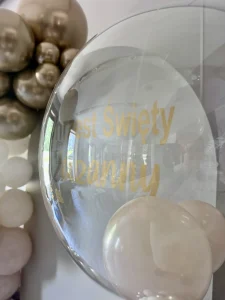 Duży, przezroczysty balon z helem wypełniony malutkimi balonikami, stanowiący elegancki dodatek do ścianki na chrzest