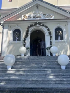 Cztery duże białe balony wybuchające ustawione na ozdobnych podstawkach przed kościołem