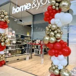 Trzymetrowe kolumny balonowe sięgające dokładnie do wysokości podświetlanego logo salonu Home & You