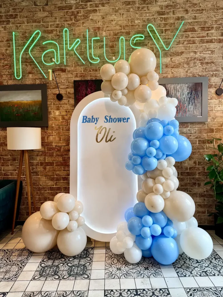 Owalna ścianka balonowa LED na Baby Shower Oli z organiczną girlandą w kolorze beżowym i baby blue, zrealizowana w restauracji Kaktusy w Katowicach